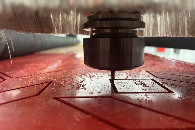 Detail vřetena CNC frézy při obrábění červené plastové desky